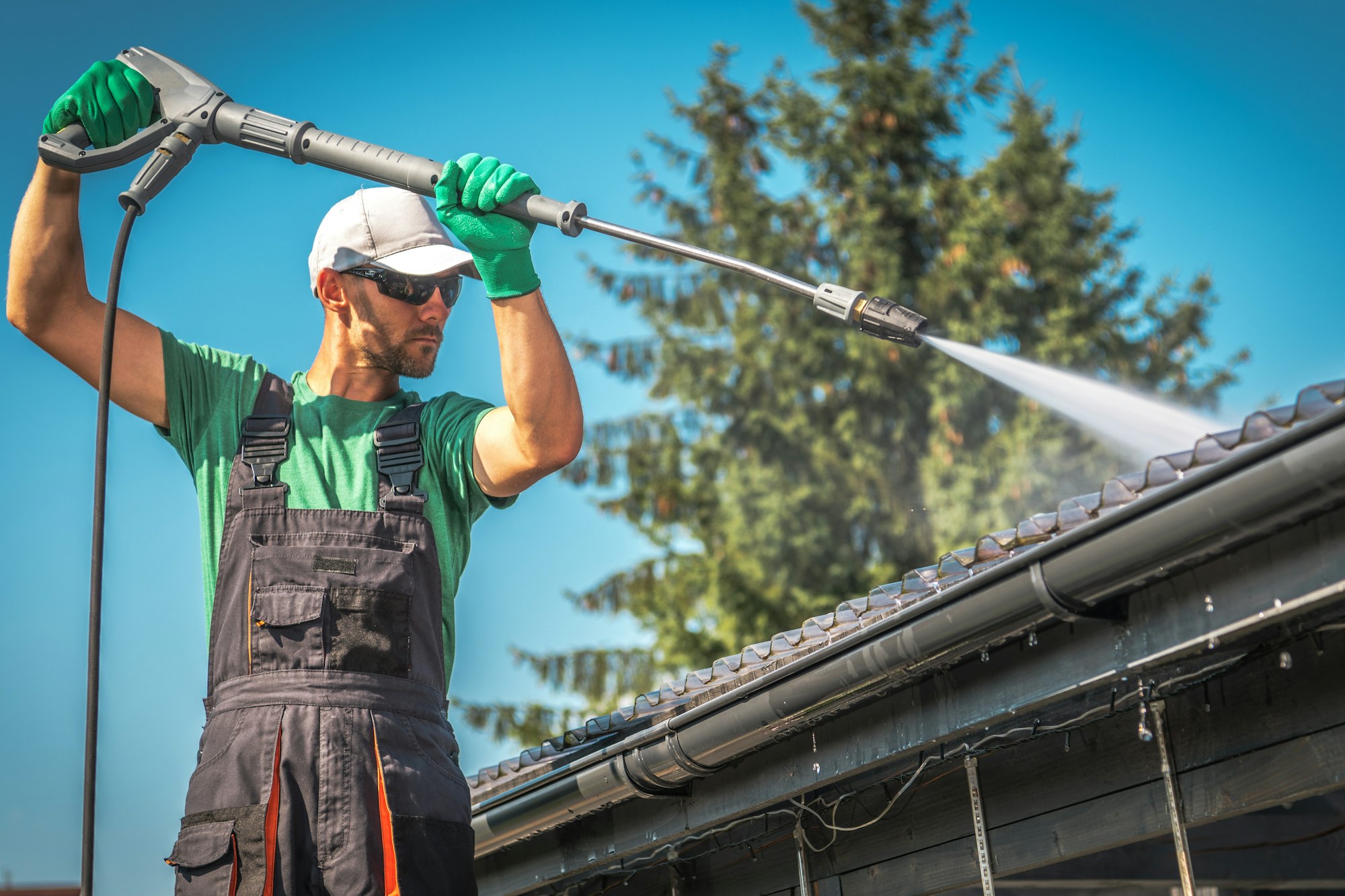 A man is pressure washing the roof of a car port.