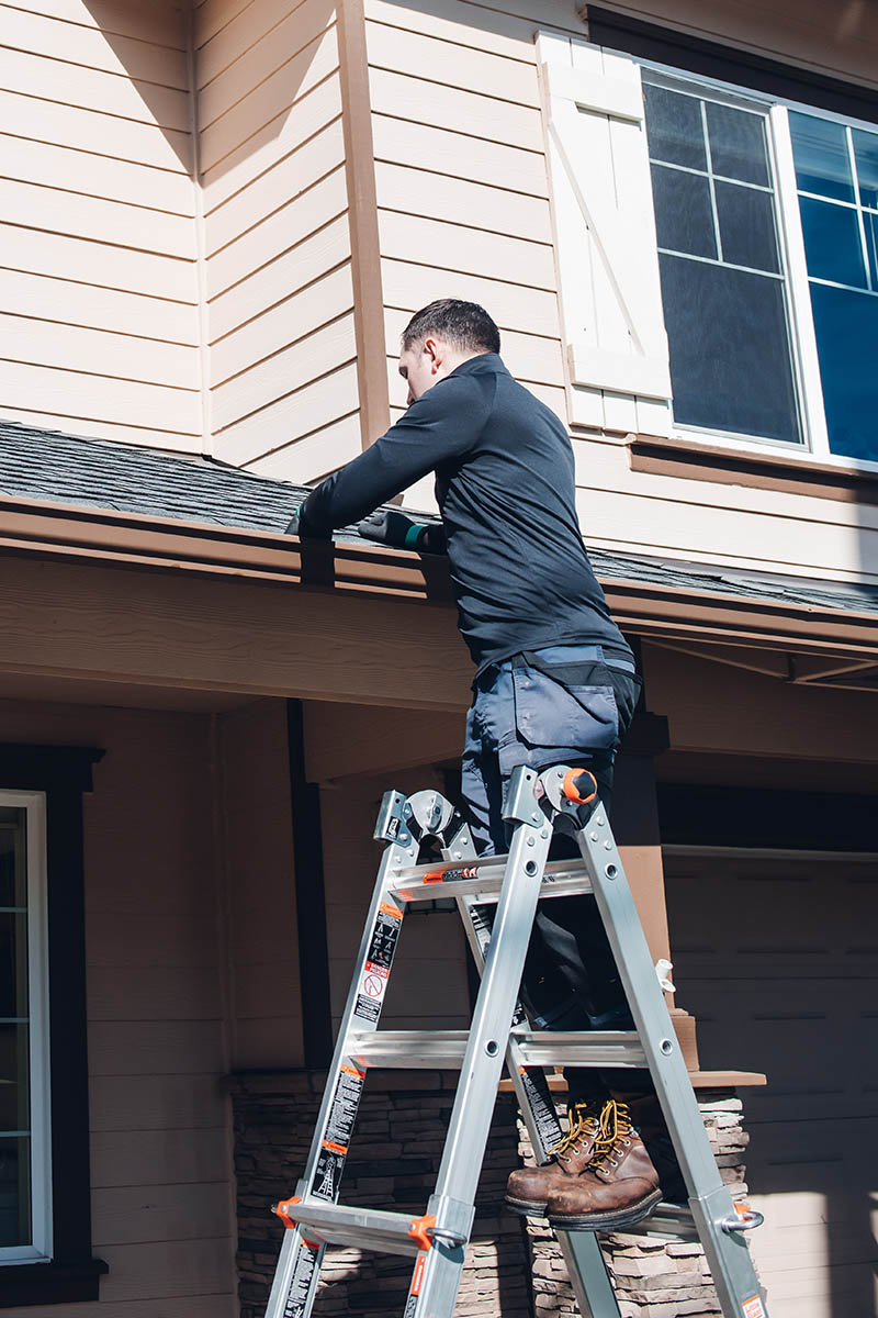 Cleaning Professional of emerald isle cleaning stands on a ladder while cleaning a client's gutters