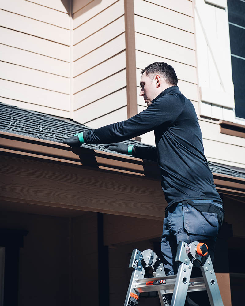 emerald isle cleaning professional stands on a ladder and cleans a client's gutters by hand