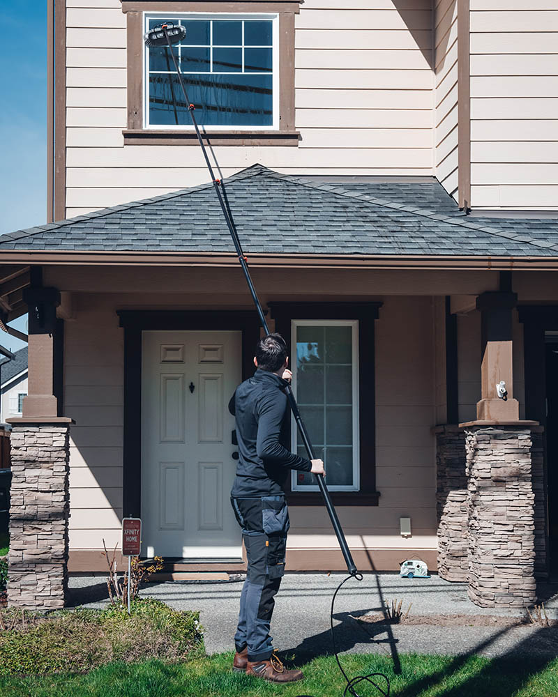 emerald isle cleaning employee pole cleans a second story window from the ground